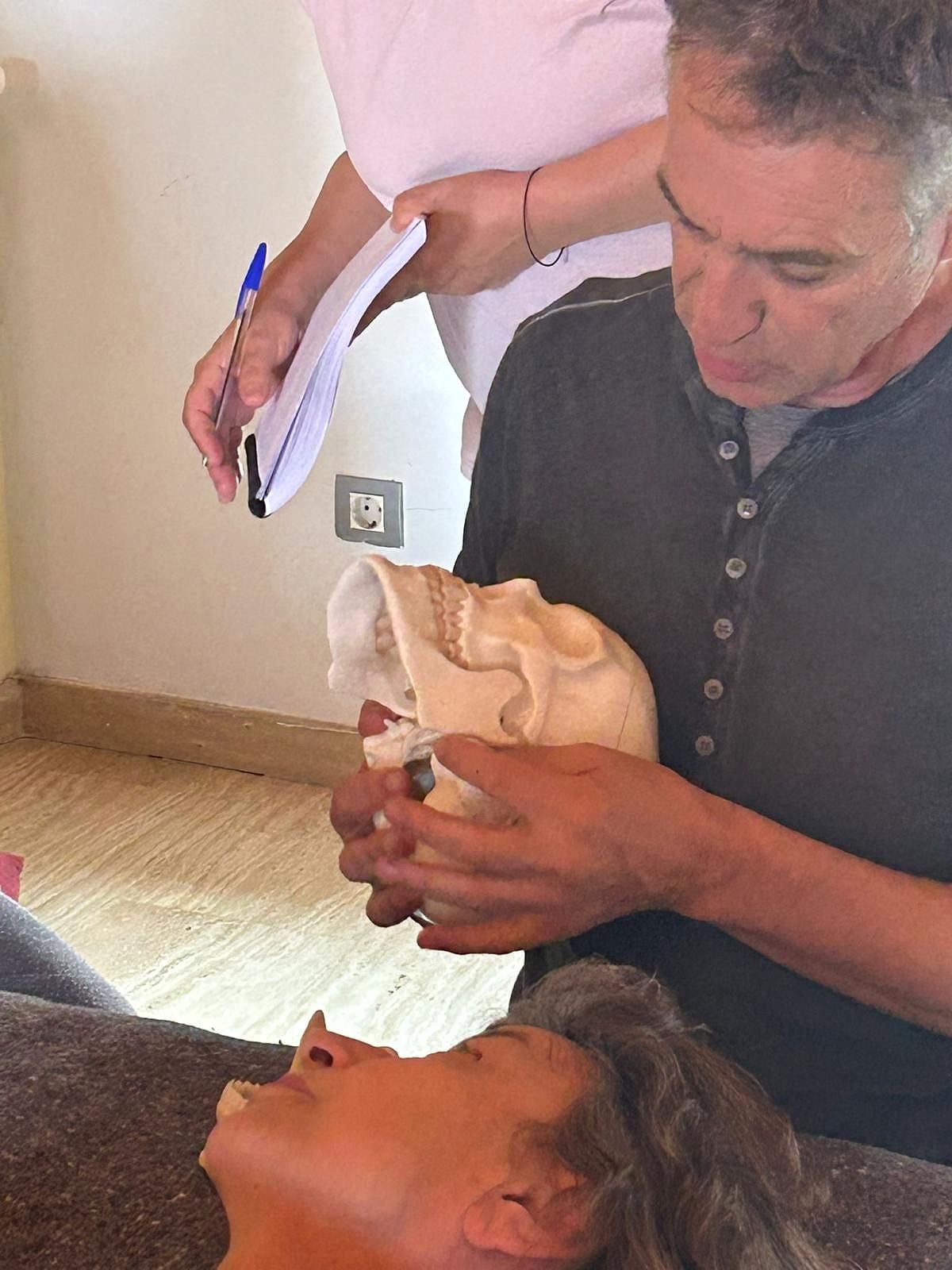 Docente mostrando un modelo anatómico de cráneo junto a una persona tumbada